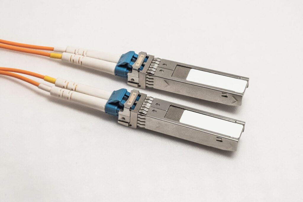 Zwei SFP-Module mit angeschlossenen Glasfaserkabeln für schnelle und zuverlässige Datenübertragung. SFP-Module sind entscheidend für den Aufbau leistungsfähiger Netzwerke in modernen Gebäuden.