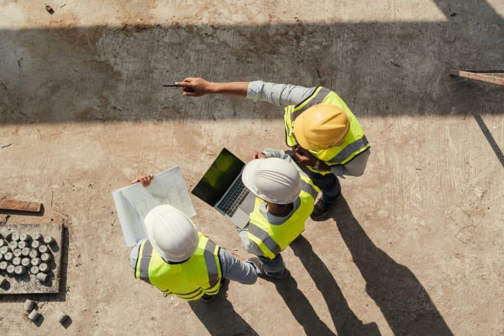 Drei Bauleiter koordinieren die baustellenreinigung direkt auf der Baustelle mit Plan und Laptop